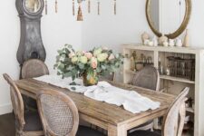 a neutral French chic dining room with a storage cabinet, a mirror, a stained vintage table, vintage chairs and a grandfather’s clock
