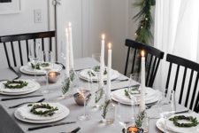 a neutral and simple winter tablescape with mini greenery wreaths for decor, candles in vases with greenery and mini tealights