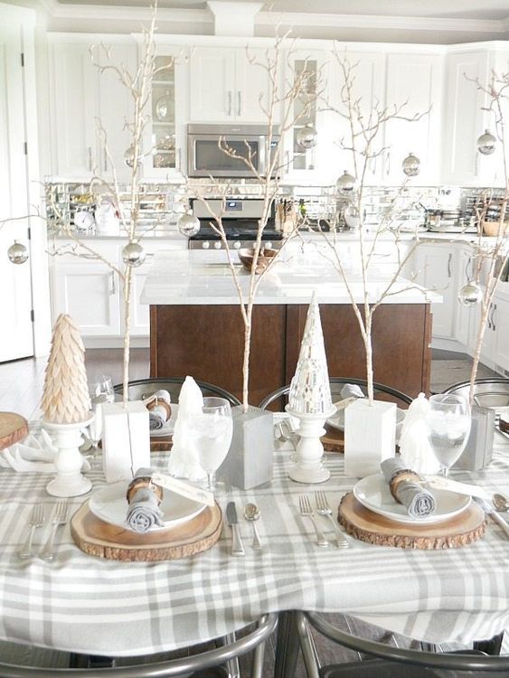 a neutral winter table with a plaid tablecloth, faux trees, mini trees with silver ornaments, wood slice placematts