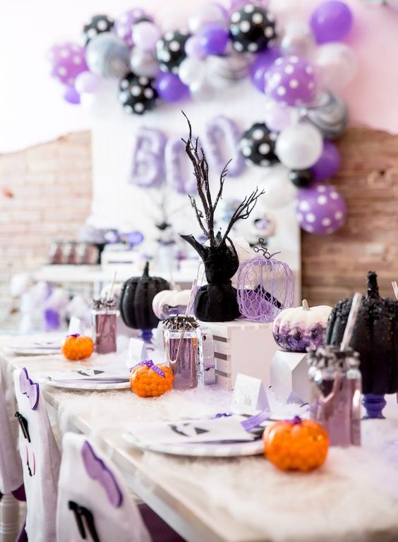 a pastel modern Halloween tablescape with black, watercolor and wire pumpkins, lavender lemonade and cutlery, candies and branches