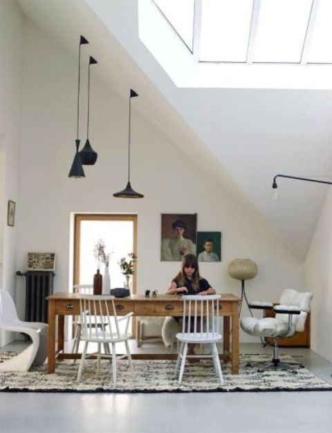 a refined eclectic attic home office with a skylight, a wooden desk, some mismatching chairs, blakc pendant lamps, refined artworks