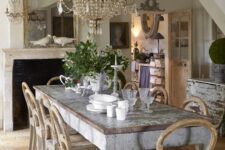 a shabby chic meets French farmhouse dining room with a statement crystal chandelier, shabby wooden furniture and greenery