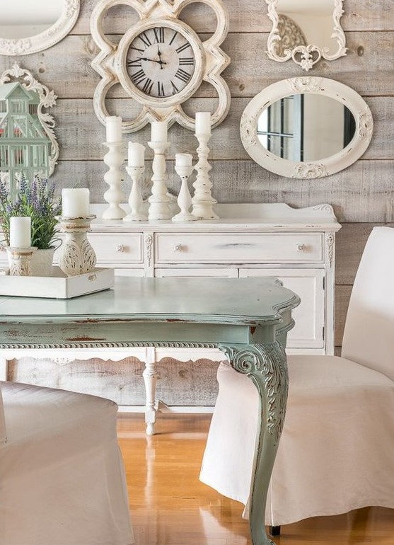 A shabby chic meets rustic dining room with rough wooden walls, a gallery wall with mirrors and art, a mint colored table and candles