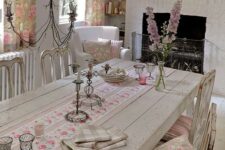 a shabby chic neutral dining room with wooden furniture, a fireplace, pink floral textiles and a vintage chandelier
