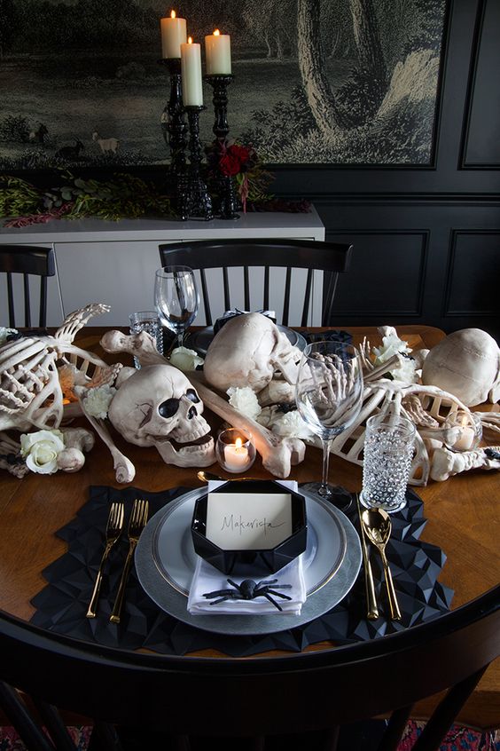 a stylish Halloween tablescape with bones, skulls, candles, white blooms, black geometric placemats and plates, gold cutlery