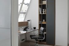 a stylish contemporary attic home office with a sleek desk, a black leather chair, some built-in storage units and a cool table lamp