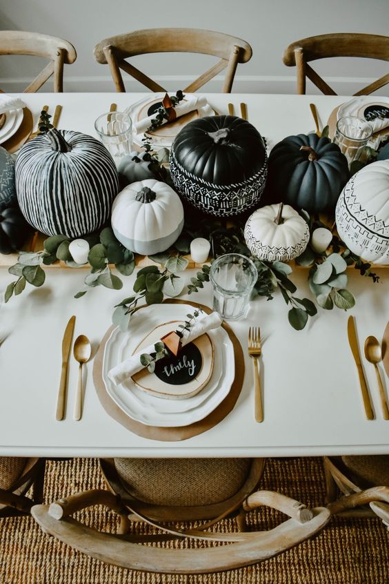 a stylish modern Halloween tablescape with grey, black and white pumpkins, eucalyptus, gold cutlery and chargers