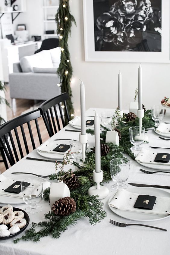 a stylish monochromatic winter table with an evergreen and pinecone runner, grey candles, white house vases, polka dot napkins