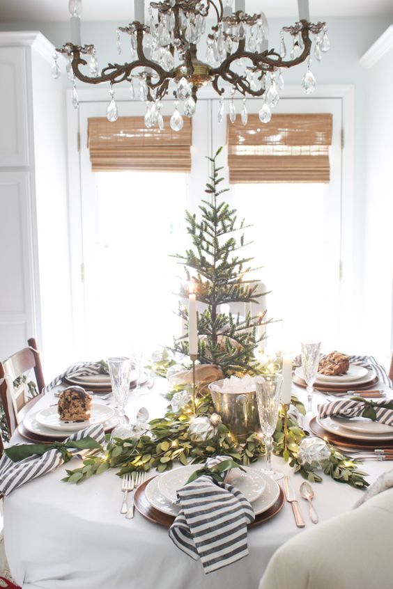 a stylish winter table with a Christmas tree, an evergreen and light runner and striped napkins