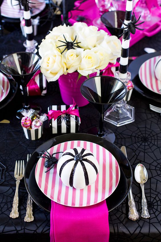 a super bright modern Halloween tablescape in black, white and hot pink, white roses, pink plates, napkins and other detailing