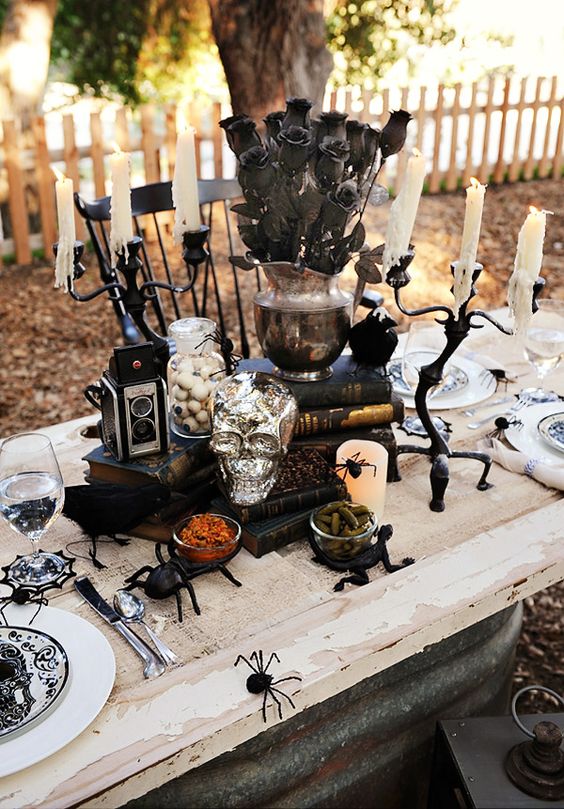 a vintage Halloween table setting with spiders, a silver skull, black blooms, vintage cameras and printed plates