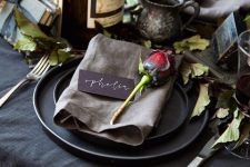 a vintage Halloween tablescape with black linens and plates, leaves and red roses, vases and candles