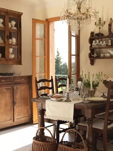 a vintage farmhouse dining room with stained furniture - a dining set, a wall-mounted shelf and some cabinets, a crystal chandelier