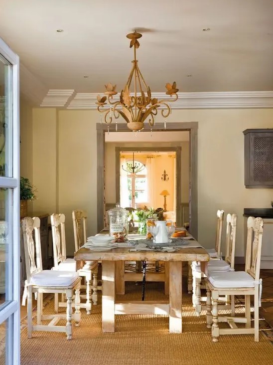A warm colored vintage rustic dining room with a stained dining table and stained chairs, a vintage chandelier, a large warm colored rug for more coziness in the space
