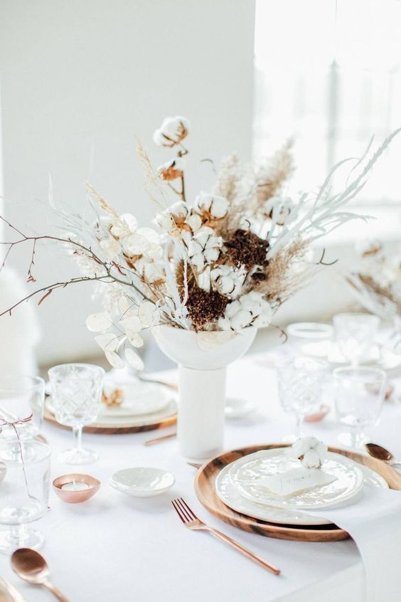 a warming up winter table with a dried herbs and cotton centerpiece, wood chargers, copper candleholders and cutlery