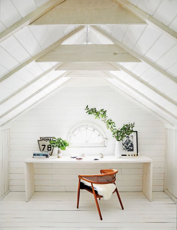 a white attic home office with wooden beams on the ceiling, a white desk, a stained chair, a small arched window is welcoming