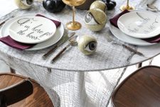 a wicked Halloween tablescape with cheesecloth, black pumpkins, white plates, purple napkins and large eyeballs