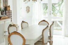 an adorable French chic dining room with a storage unit, vintage artworks, a white vintage table, vintage chairs and a chic chandelier