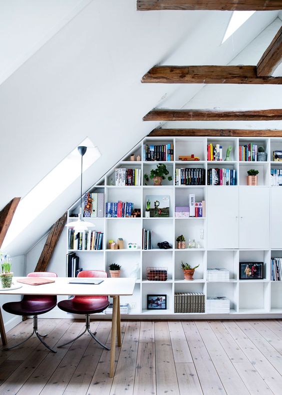 An attic home office with stained wooden beams, a built in storage unit, a desk, pink and purple chairs and some skylights to give more natural light