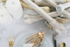 an elegant white and gold Halloween tablescape with bones, white spiders, candles, gold skeleton hands and glass plates