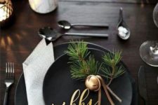 an elegant winter tablescape with black plates, bells with evergreens, bulbs in pots and candles