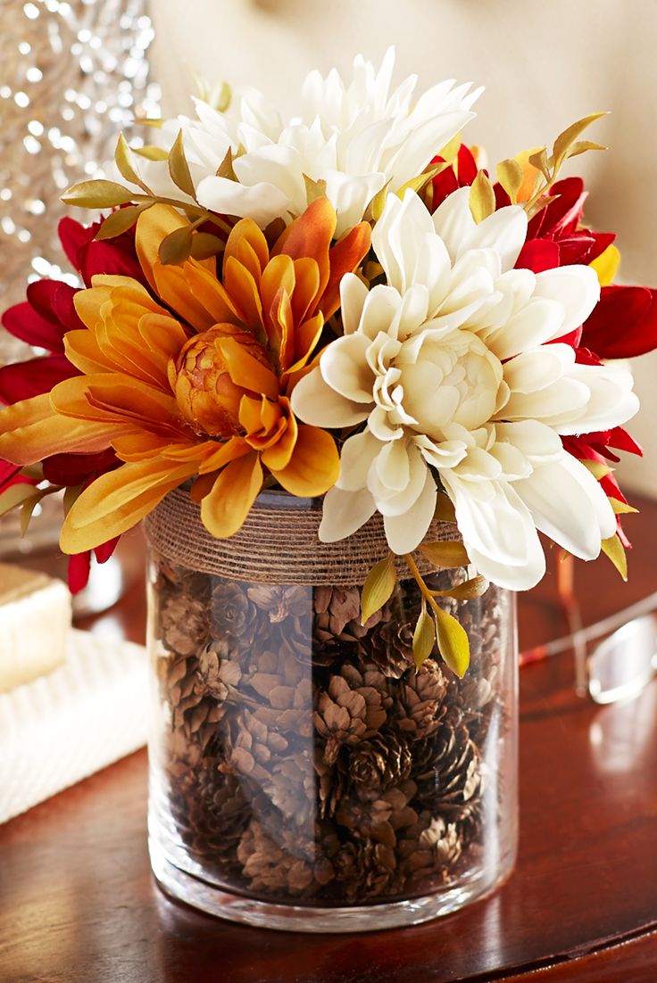For a tabletop focal point mix faux dahlias in a vase filled with pinecones.