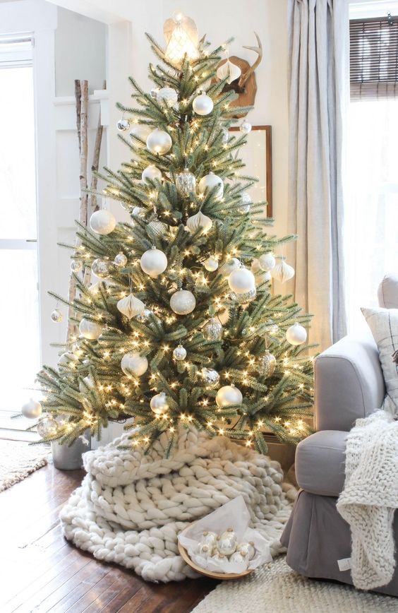 a Christmas tree with lights, silver and white ornaments plus a shiny lamp on top