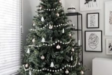 a Christmas tree with white and metallic ornaments and pompoms garlands and black and white gift boxes