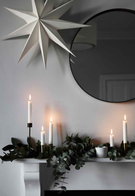 a mantel decorated with eucalyptus, white candles and a large paper star over it all for a Nordic feel