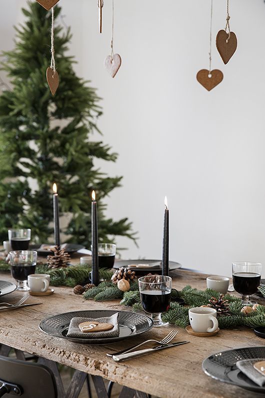 a modern Scandinavian table with evergreens, pinecones, black candles and porcelain, gingerbread cookies and simple cups