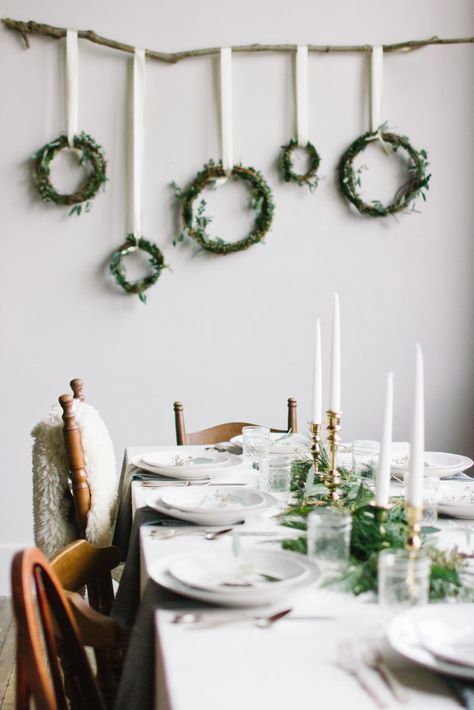 a modern and fresh Nordic table with greenery, gold candleholders, white porcelain and an arrangement of wreaths on the wall