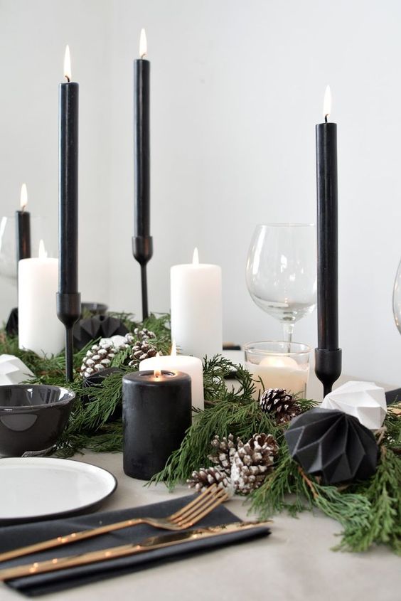 a monochromatic Scandinavian tablescape with black and white candles, evergreens, pinecones and white porcelain