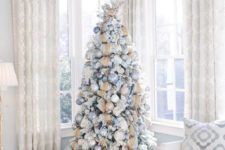 a snowy Christmas tree with blue, silver and tan ornaments plus burlap ribbons and a large branch topper