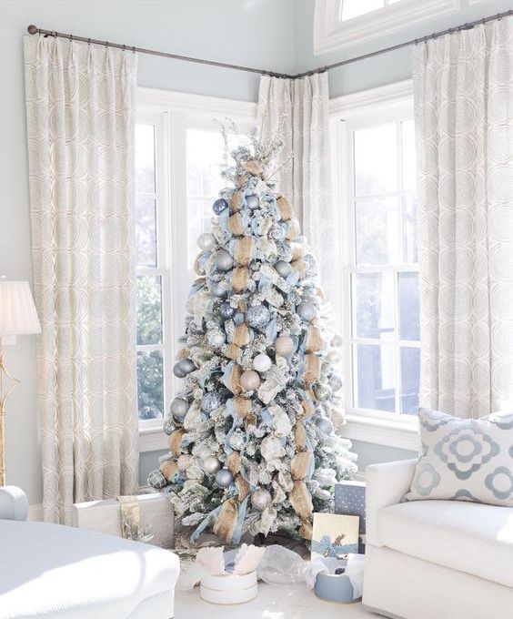 a snowy Christmas tree with blue, silver and tan ornaments plus burlap ribbons and a large branch topper
