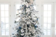 a snowy Christmas tree with white and bold blue ornaments and striped ribbons plus a burlap skirt