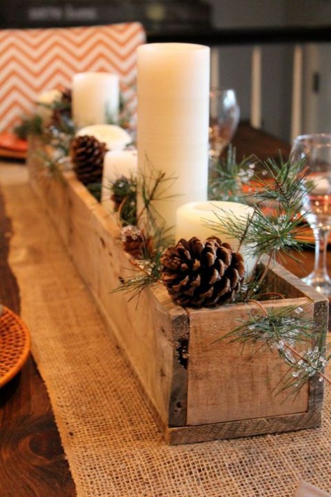a Christmas centerpiece of a wooden box, evergreens, pinecones and pillar candles is very cozy