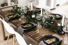 a Nordic rustic tablescape with an evergreen runner, pinecones, candles, black plates and grey napkins