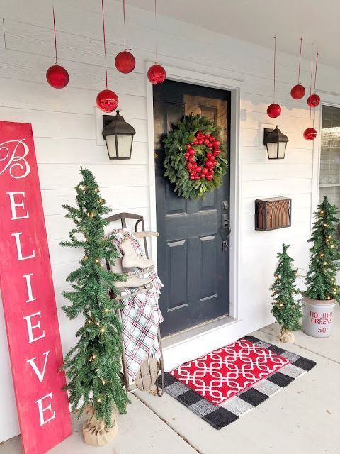a bright and fun Christmas porch with red ornaments, mini lit up Christmas trees, a red sign and layered mats
