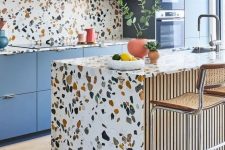 a bright kitchen with blue cabinetry, terrazzo countertops, a backsplash and a kitchen island and coral pendant lamps is amazing