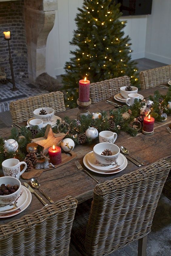 a chic Christmas tablescape with an evergreen and ornament runner, pillar candles, wooden stars and pinecones