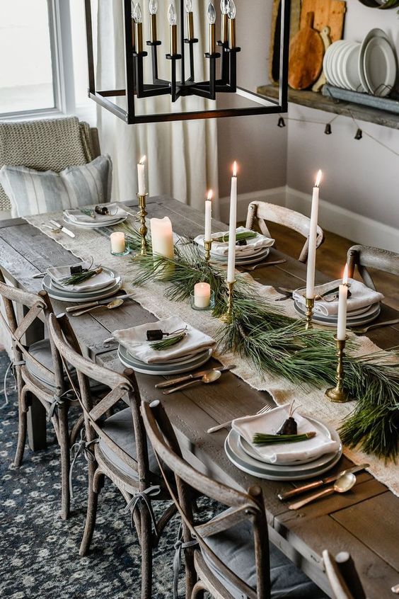 a chic rustic Christmas table with a burlap runner, porcelain plates, tall candles and an evergreen runner