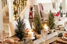 a chic rustic Christmas tablescape with a burlap runner, placemats, mini potted trees, candles and plaid napkins