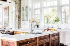 a farmhouse white kitchen with a unique vintage rich-stained wooden kitchen island and a large metal chandelier looks wow