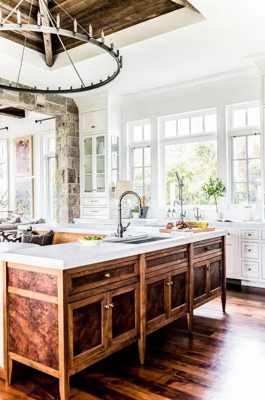 A farmhouse white kitchen with a unique vintage rich stained wooden kitchen island and a large metal chandelier looks wow