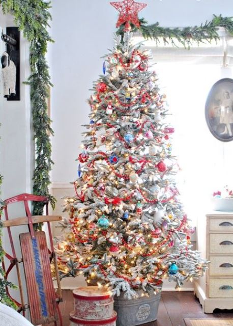 A flocked Christmas tree with colorful ornaments, lights and a red yarn star tree topper looks really vintage like