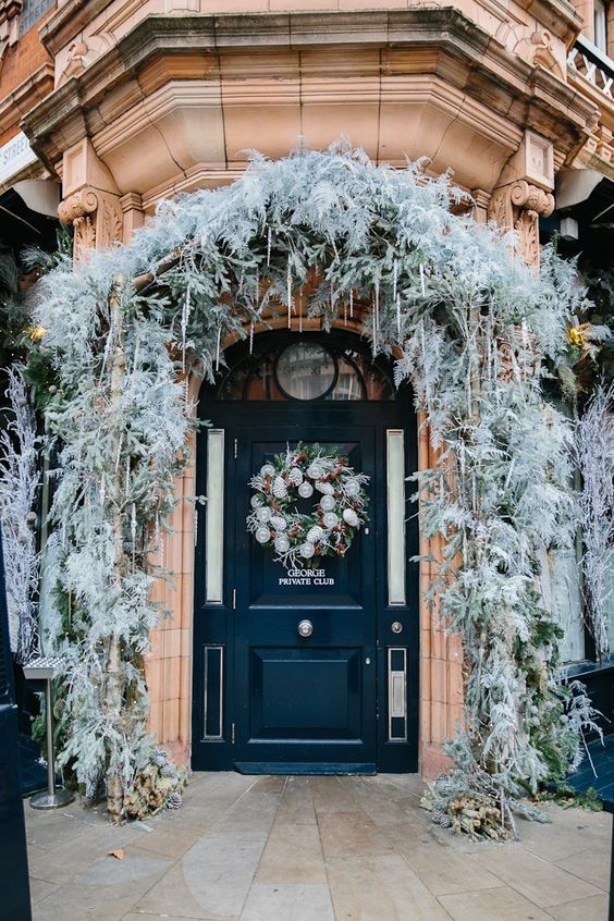 a frozen Christmas porch with pale leaves and greenery, icicles, lights, a wreath with lights and pinecones is lovely