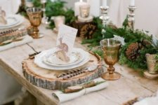 a gorgeous rustic Christmas table with an evergreen and pinecone runner, amber glasses, wood slice placemats, tall candles and deer cards