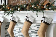 a large wooden plank Christmas sign, an evergreen garland with vine balls, pinecones and stockings of felt