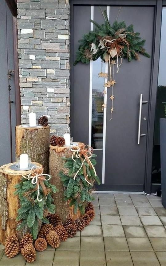 a modern woodland Christmas porch with tree stumps, evergreens, pinecones, candles and a matching posie on the door