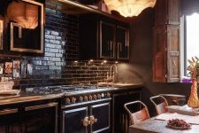a moody and glam kitchen with black cabinetry, metallic patterns, a black tile backsplash, a unique pendant lamp, a rough table and leather chairs